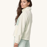 An adult wearing the Patagonia Women's Microdini 1/2 Zip Fleece Pullover - Birch White with a light blue pocket and zips