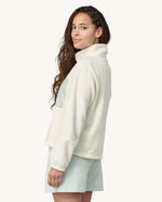 An adult wearing the Patagonia Women's Microdini 1/2 Zip Fleece Pullover - Birch White with a light blue pocket and zips