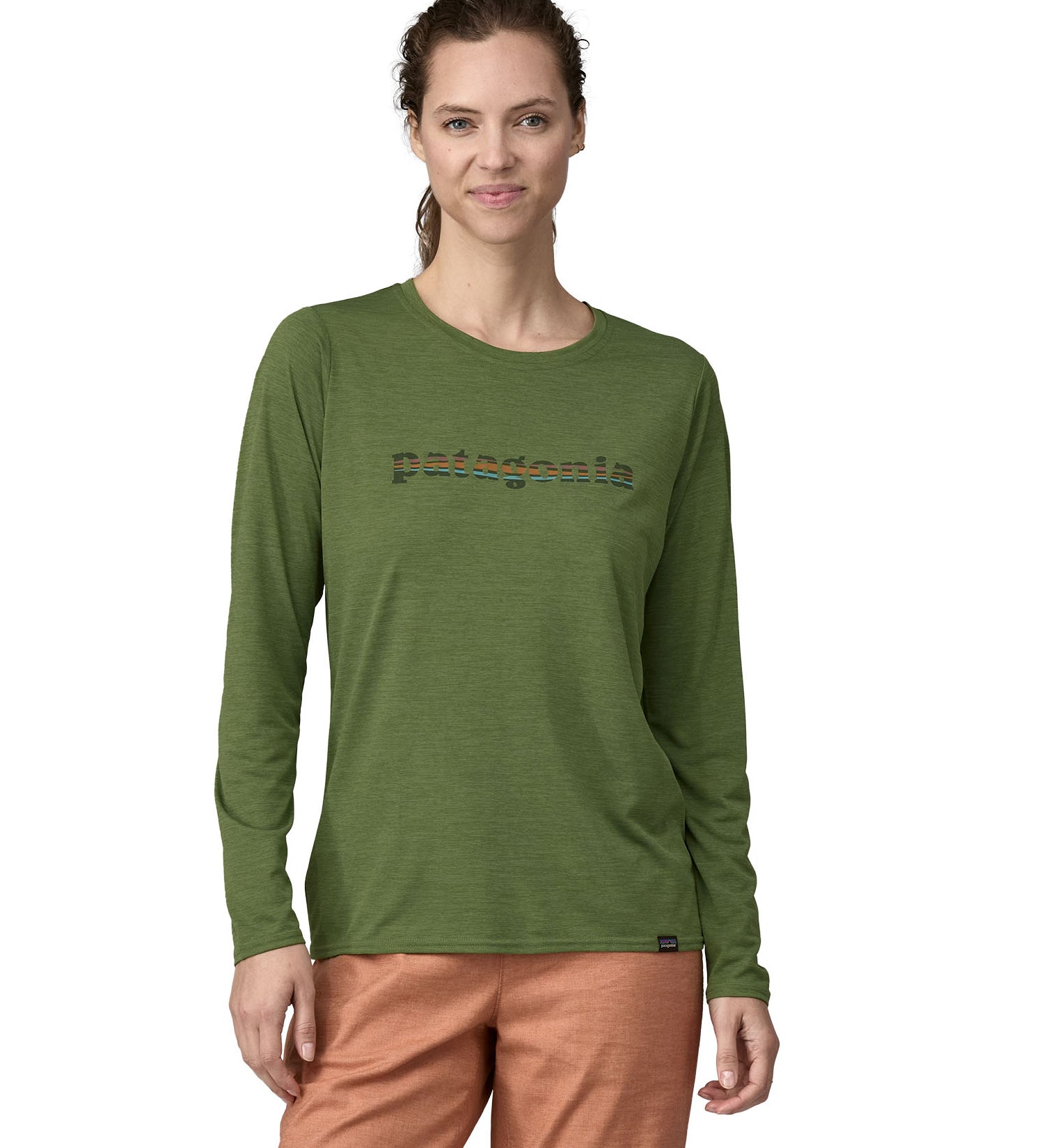 A woman wearing a Patagonia Women's long sleeved Cap Cool Daily Graphic Shirt in a Green X-Dye colour. The woman is stood in front of a plain background. 