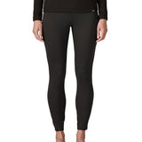 Woman wearing the Patagonia women's Capilene midweight bottoms black. Fitted leggings sitting on the ankles. 