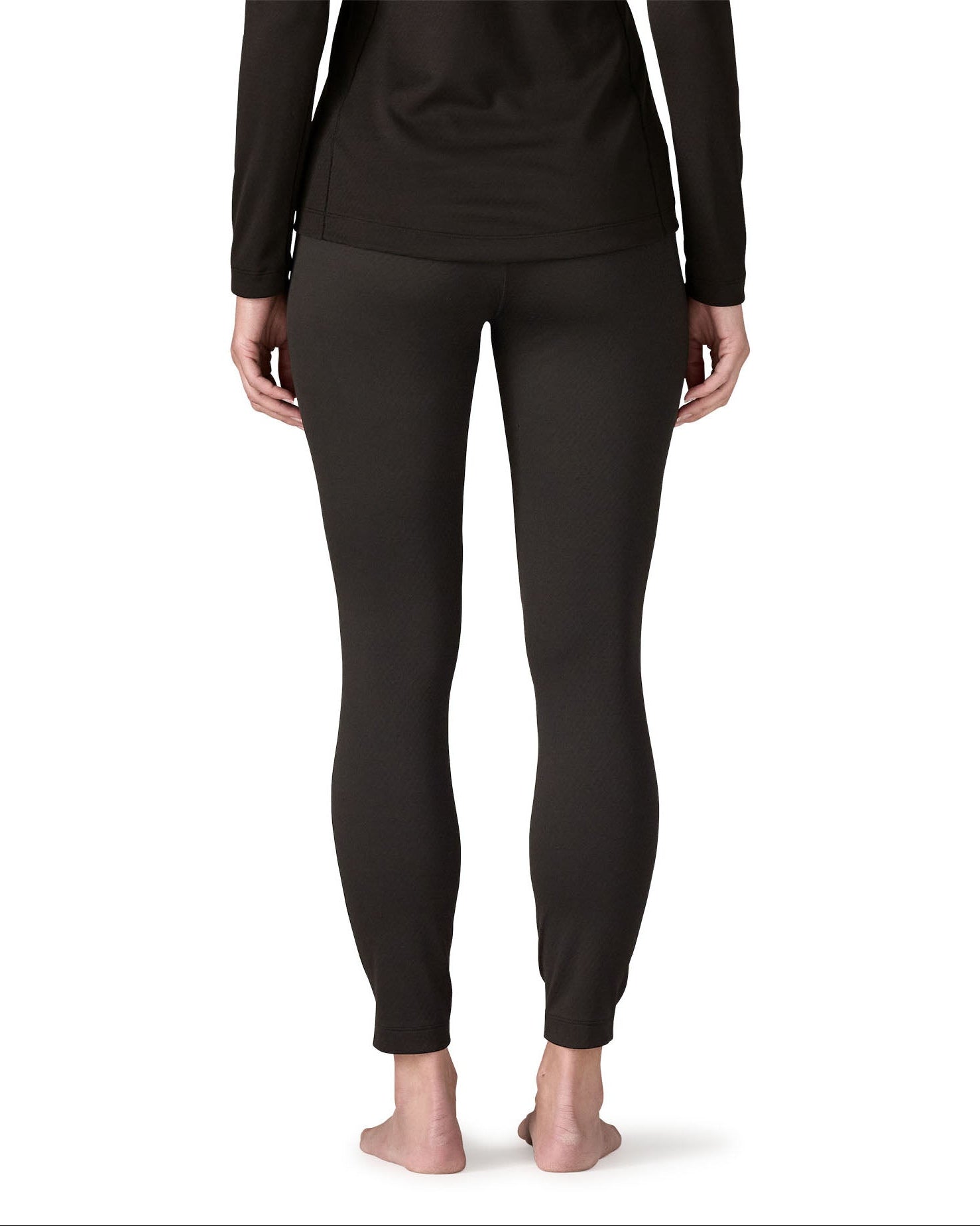 Back of woman wearing the Patagonia women's Capilene midweight bottoms black. Fitted leggings sitting on the ankles. 