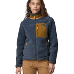 A woman wearing a Patagonia Women's Classic Retro-X jacket in a Utility Blue colour. The front zip of the jacket is fully closed. 