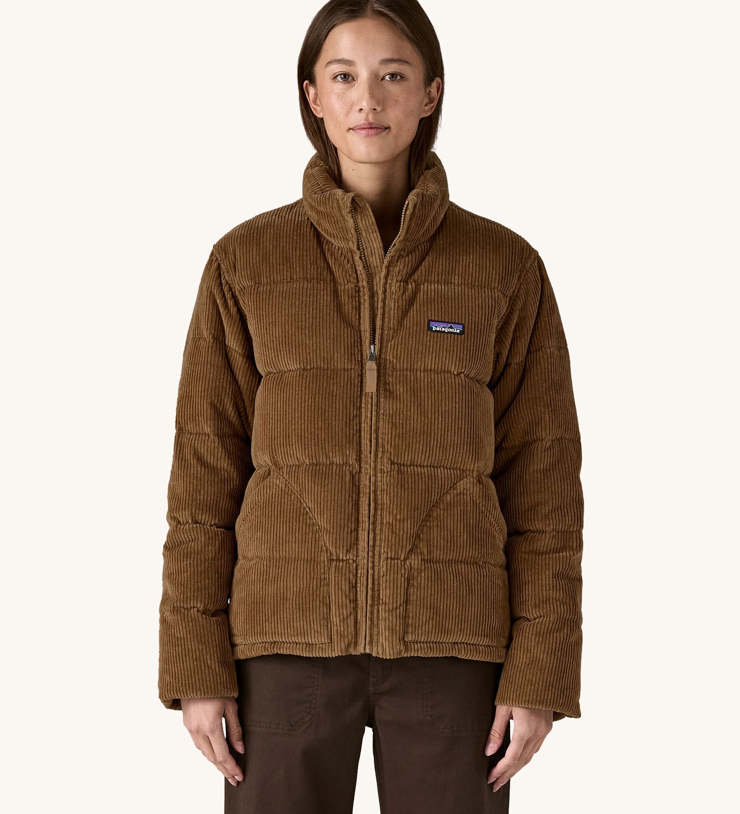 A woman wearing the Patagonia Women's Cord Fjord Down Insulated Jacket in a Deer Brown colour. We have a wide range of Patagonia adult's and children's coats and clothing at Babipur.