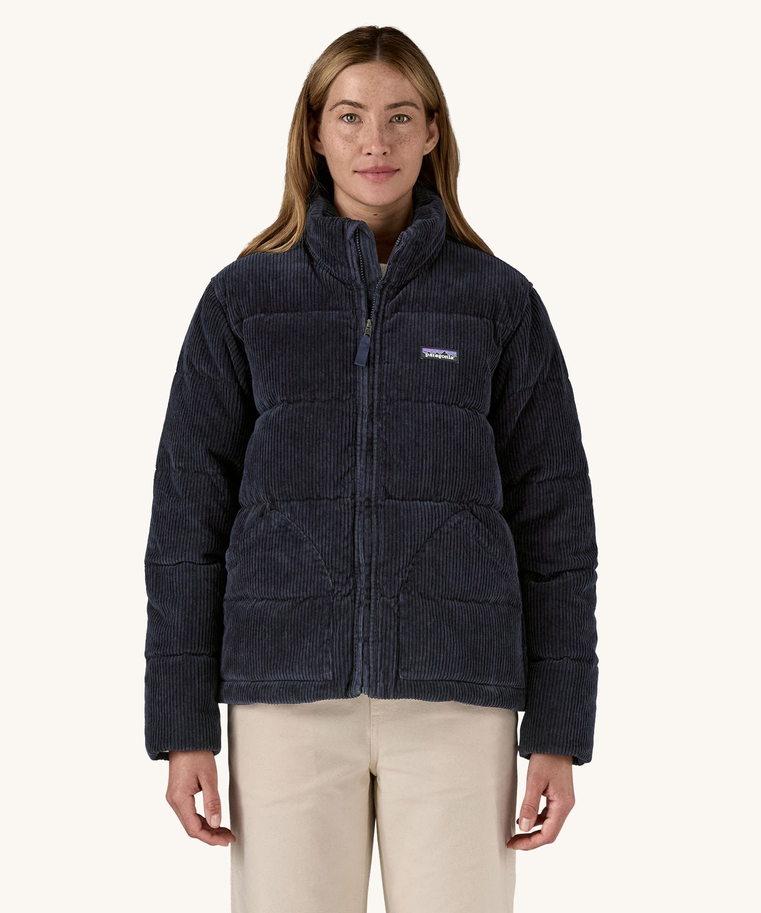 A woman wearing the Patagonia Women's Cord Fjord Down Insulated Jacket in a Sunken Blue colour. The zip is 3/4 closed. 