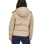 A view of the back of a woman with dark coloured shoulder length wavy hair wearing the Patagonia Women's Downdrift Jacket in Oar Tan