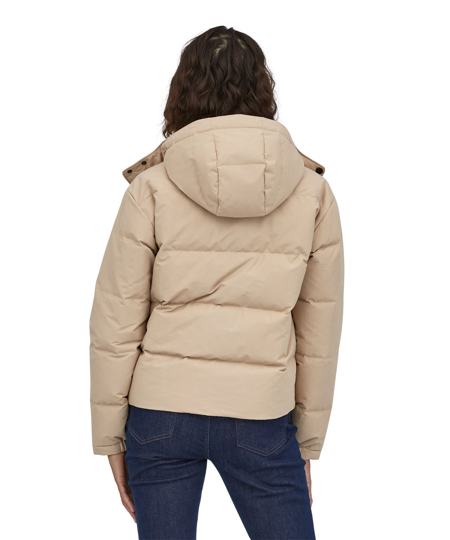A view of the back of a woman with dark coloured shoulder length wavy hair wearing the Patagonia Women's Downdrift Jacket in Oar Tan
