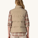 A view from the back of a woman wearing a beige coloured Patagonia Women's Downdrift Vest gilet. 