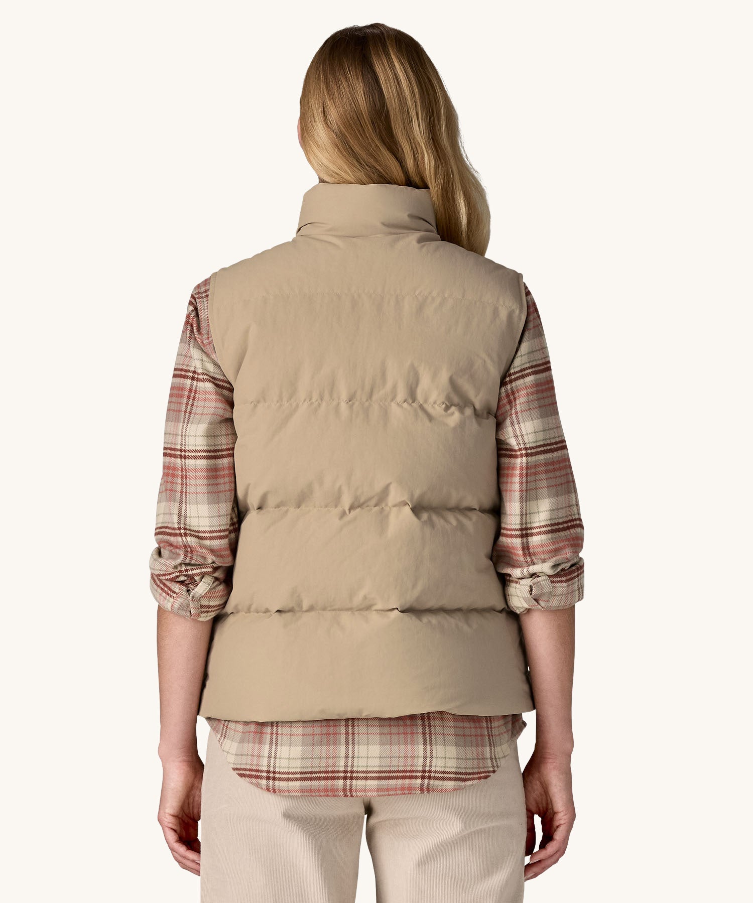 A view from the back of a woman wearing a beige coloured Patagonia Women's Downdrift Vest gilet. 