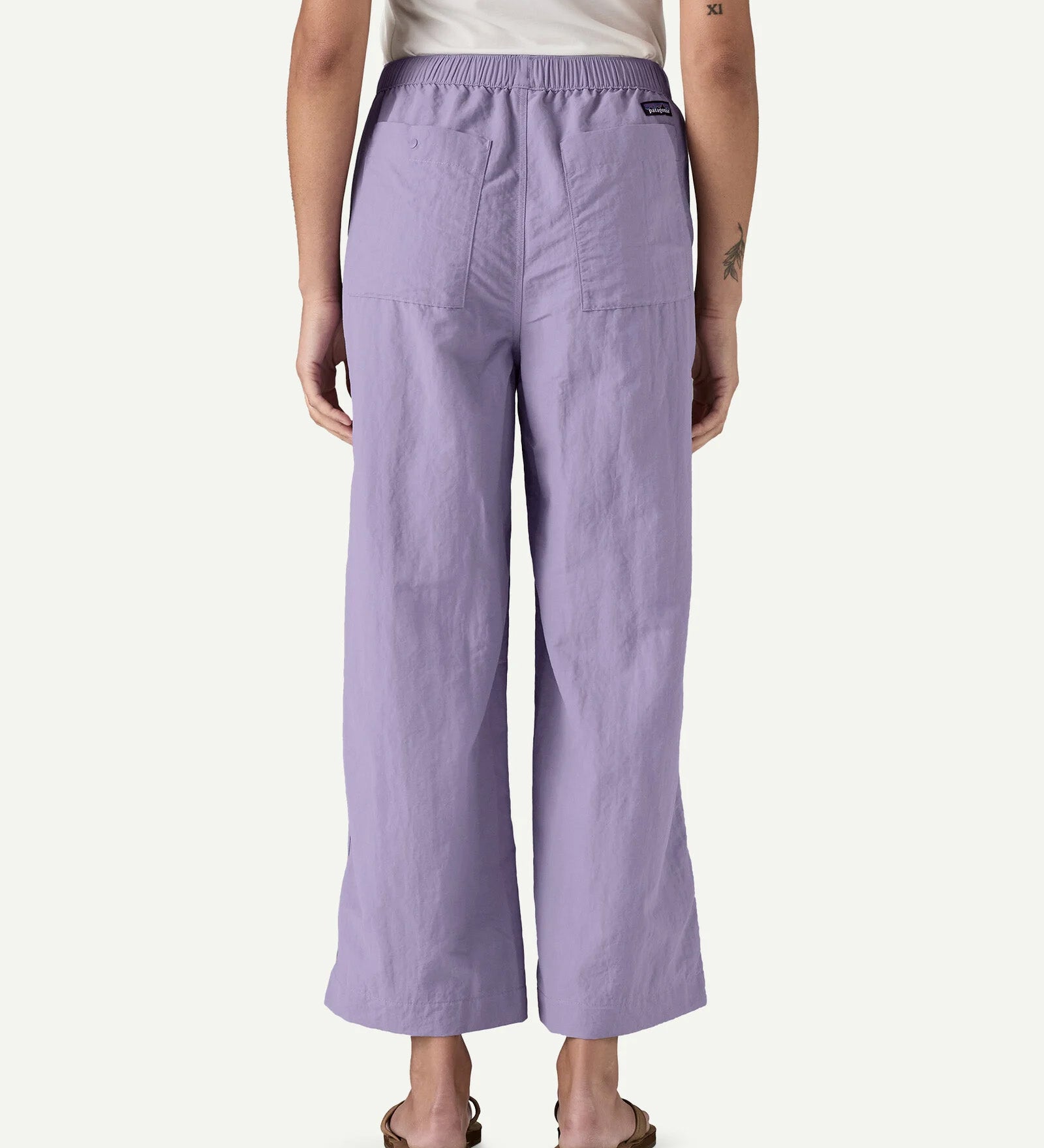 Back view of a model wearing Patagonia Women’s Outdoor Everyday Pants in purple, shown to demonstrate fit and length, with a high-rise elasticated waistband, wide-leg cropped cut, and two rear patch pockets.
