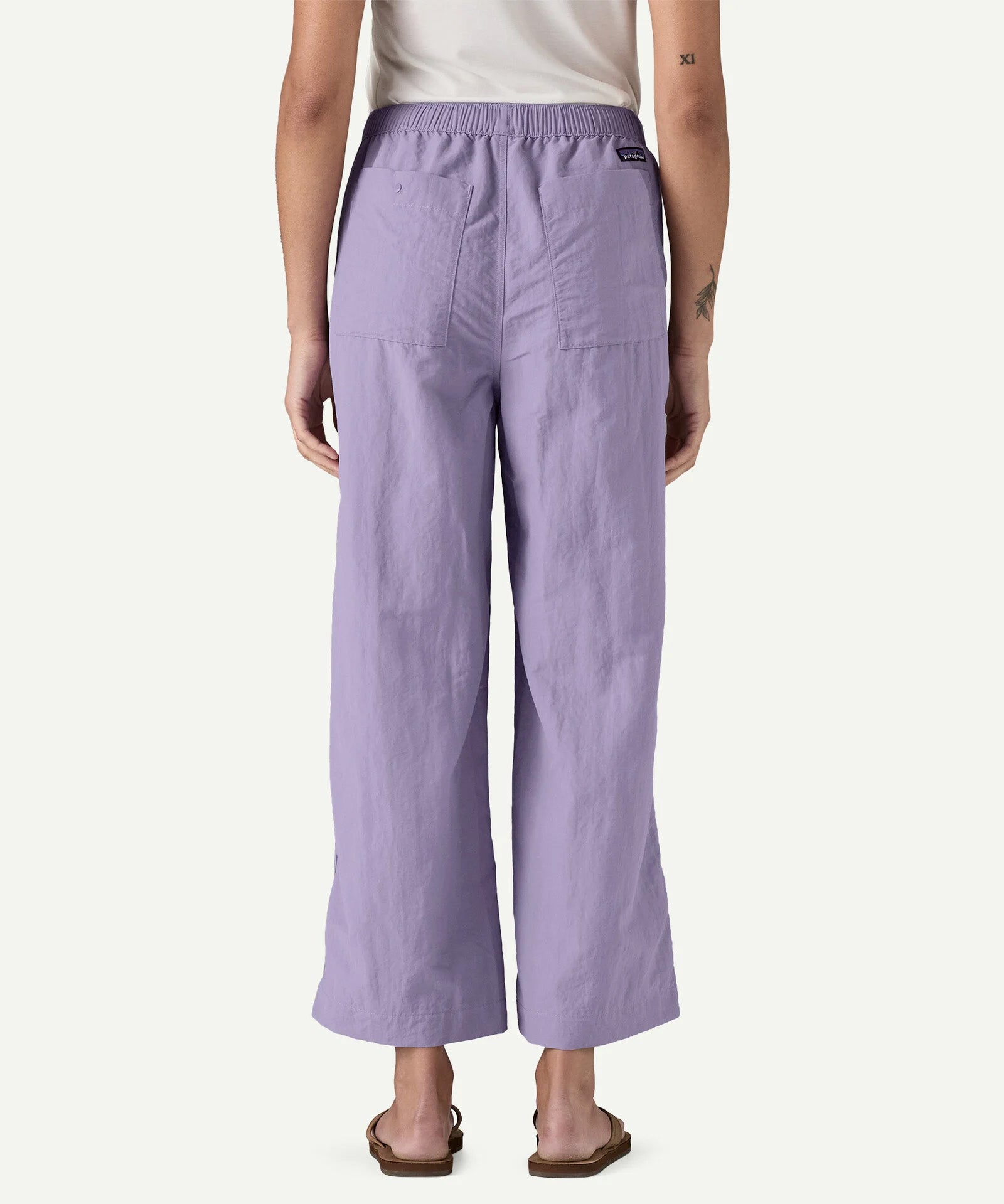 Back view of a model wearing Patagonia Women’s Outdoor Everyday Pants in purple, shown to demonstrate fit and length, with a high-rise elasticated waistband, wide-leg cropped cut, and two rear patch pockets.