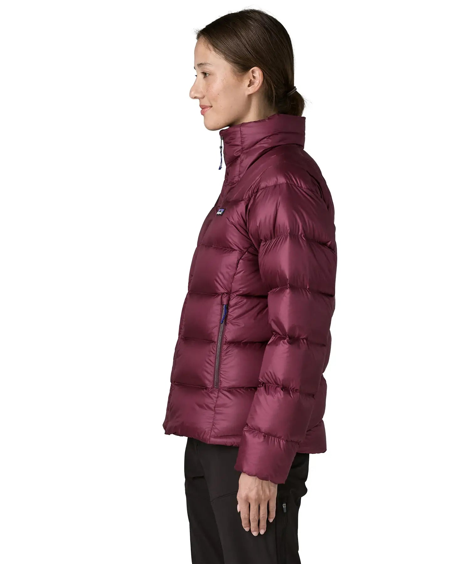 Side of woman wearing Patagonia women's fitz roy down insulated lightweight jacket in berry fig with two zippered handwarmer pockets with front zip fully closed.