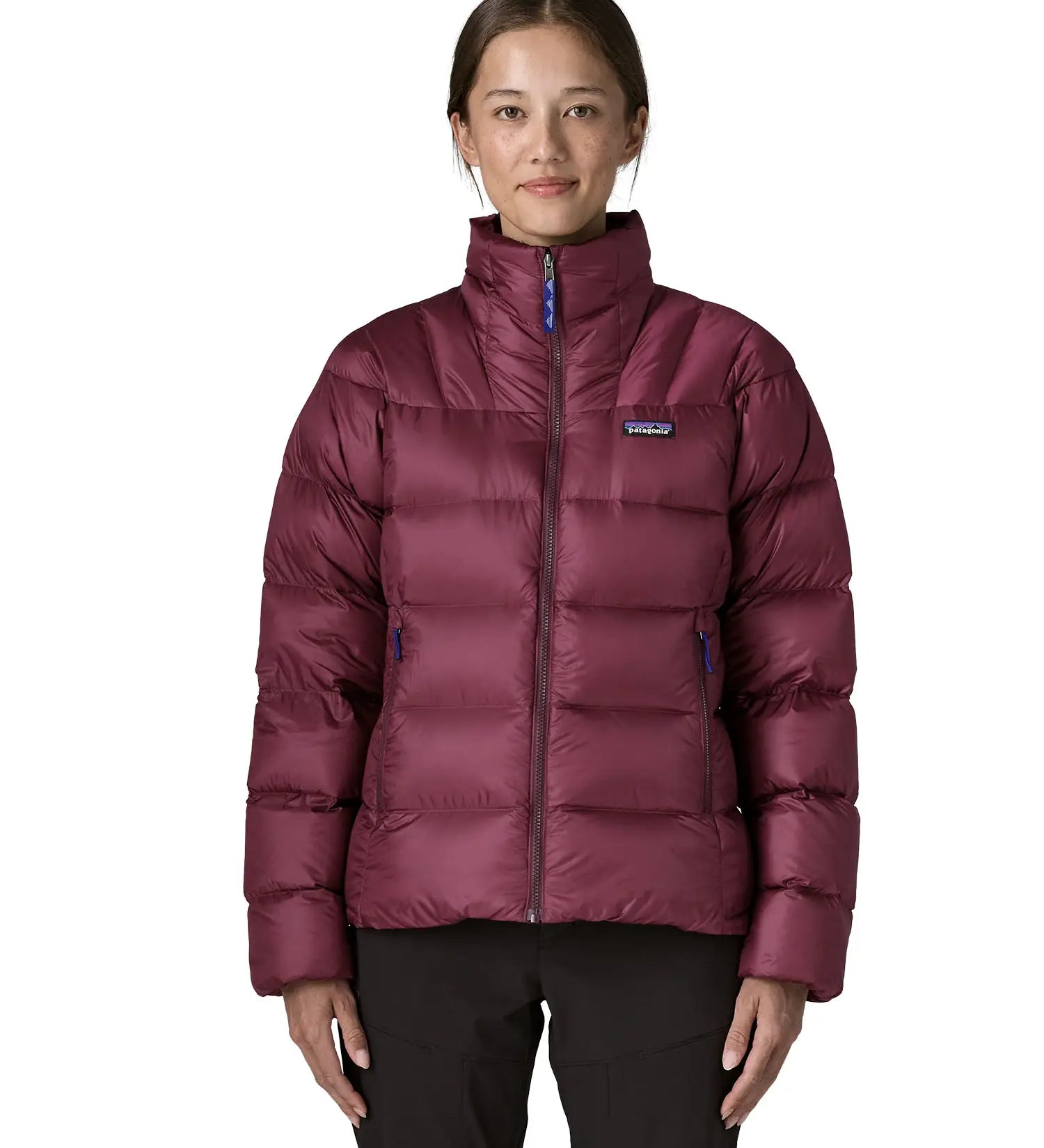 Woman wearing Patagonia women's fitz roy down insulated lightweight jacket in berry fig with two zippered handwarmer pockets with front zip fully closed.