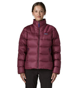 Woman wearing Patagonia women's fitz roy down insulated lightweight jacket in berry fig with two zippered handwarmer pockets with front zip fully closed.