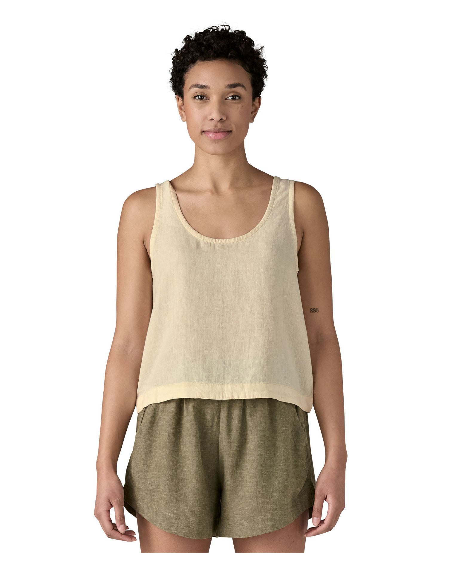 Woman wearing a Patagonia women's sleeveless loose fit top in light cream that sits just below the hip with a dipped side hem.