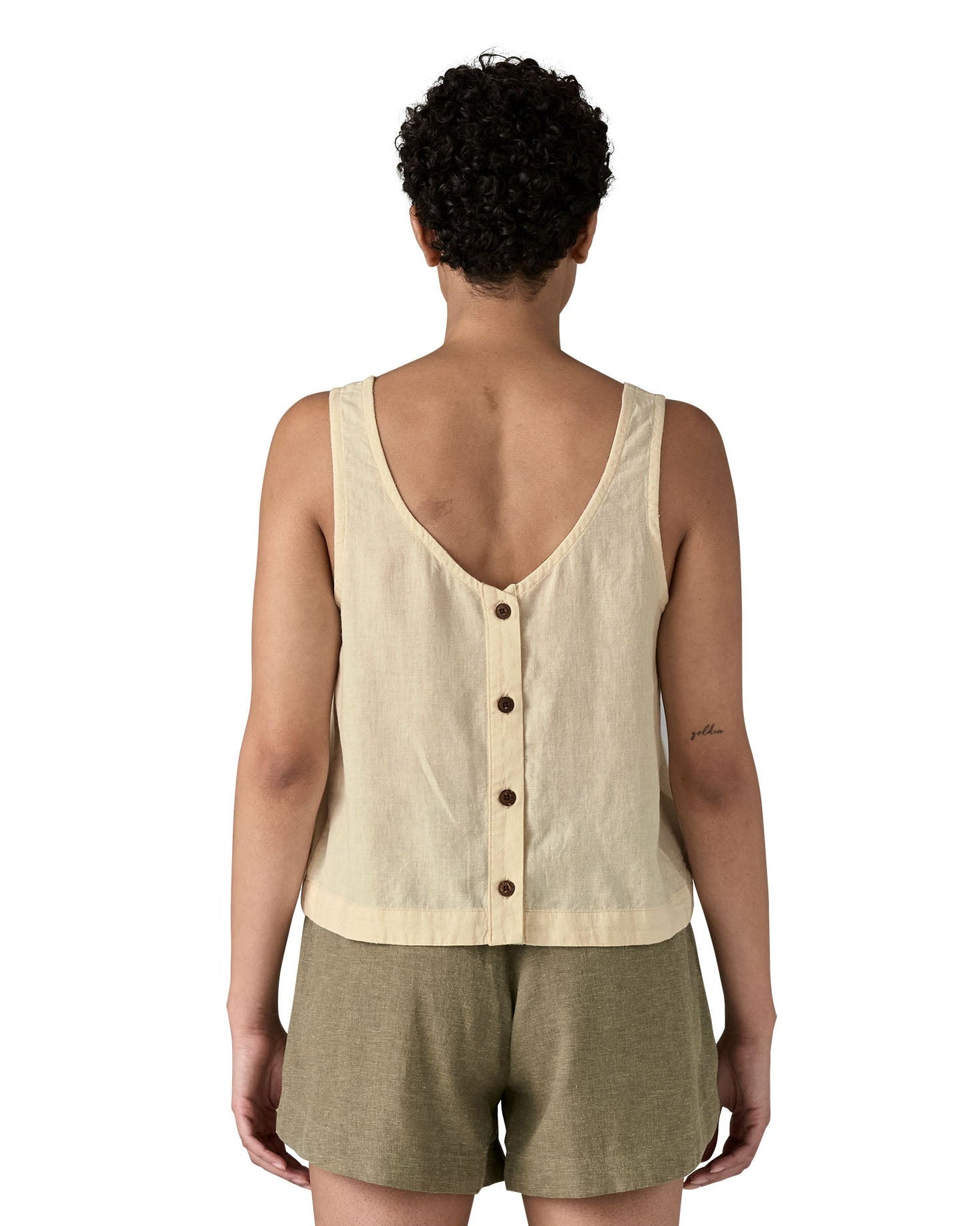 Woman wearing a Patagonia women's sleeveless garden island top in light cream whole weave material with the button up closure on the back.