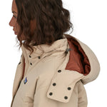 A side profile view of a woman wearing the Patagonia Women's Downdrift Jkt Oar Tan. The hood with a dark orange coloured lining can be seen along with the detachable zipped hood details