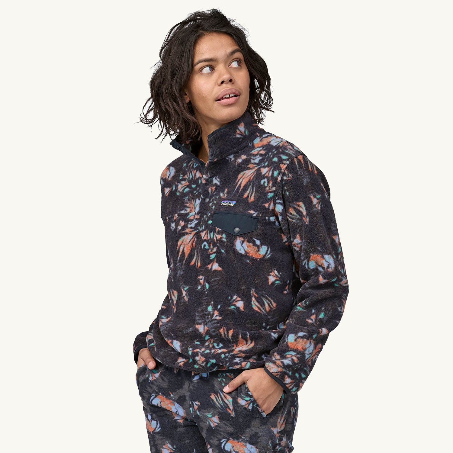 A woman models the Patagonia Women's Lightweight Synchilla Snap-T Fleece Pullover - Swirl Floral / Pitch Blue against a plain background.