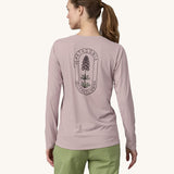 A woman wearing the back of the Patagonia Women's Long-Sleeved Capilene Cool Shirt with a  Clean Climb Bloom graphic in an Echo Purple colour showing the back of the top.