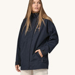 A woman wearing a Patagonia Women's Outdoor Everyday Rain Jacket in a Pitch Blue colour. The zip of the coat is fully closed.
