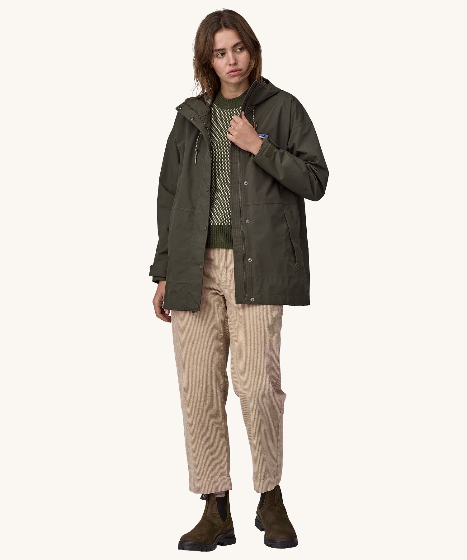 A woman wearing a Patagonia Women's Outdoor Everyday Rain Jacket in a Pine Needle Green colour. The zip of the coat is fully open.