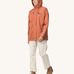 A woman wearing the Patagonia Women's Outdoor Everyday Rain Jacket in a Sienna Clay colour.