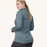 A woman models the back of the Patagonia Women's R1 Daily Jacket - Light Plume Grey / Steam Blue X-Dye against a plain background.