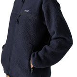 Woman wearing the Patagonia women's retro pile fleece jacket in sunken blue with zippered chest pocket with hands in the handwarmer pockets. Close up view.