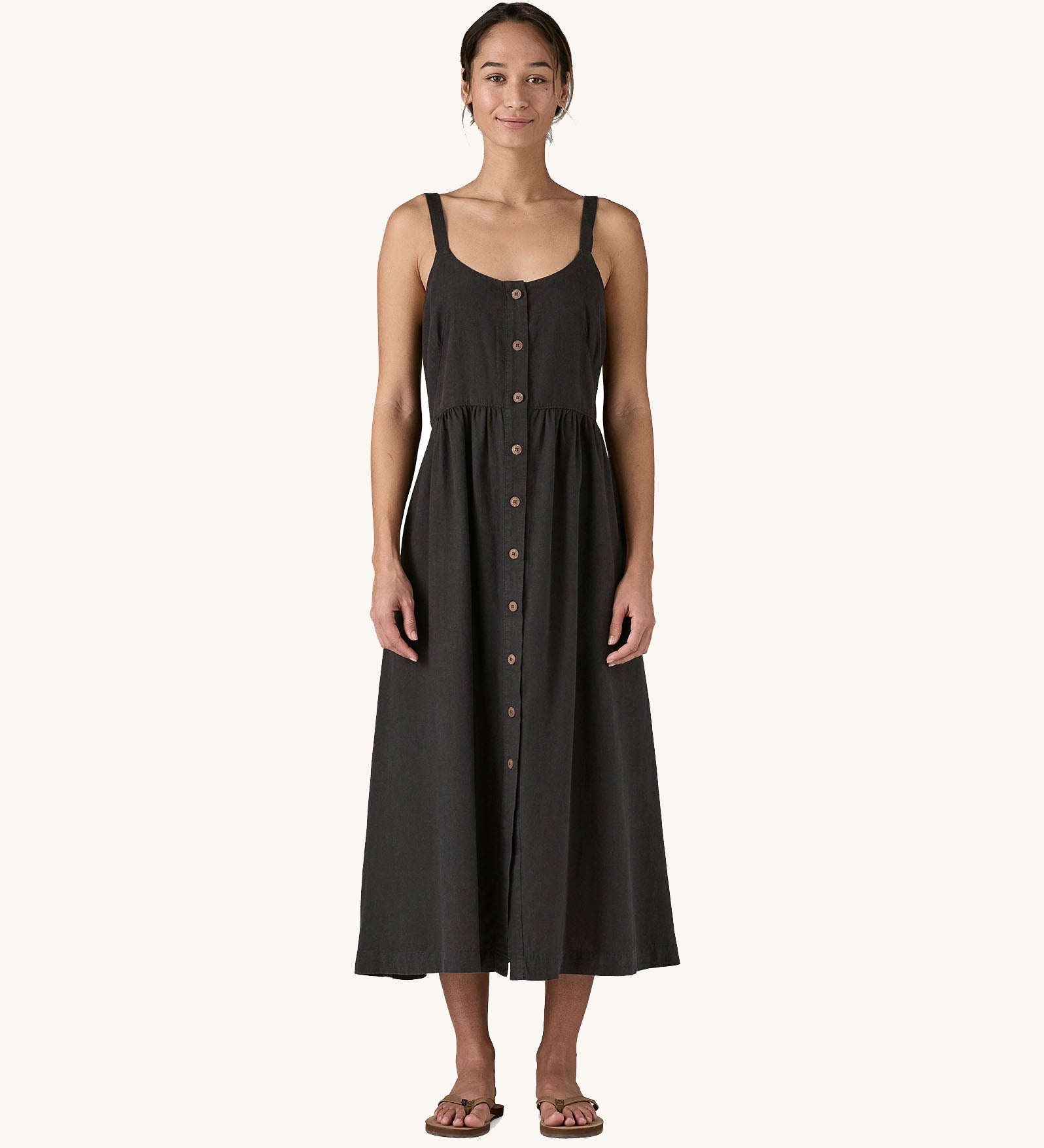 The Patagonia women's garden island dress in black being worn. This strappy dress has 10 buttons on the front.