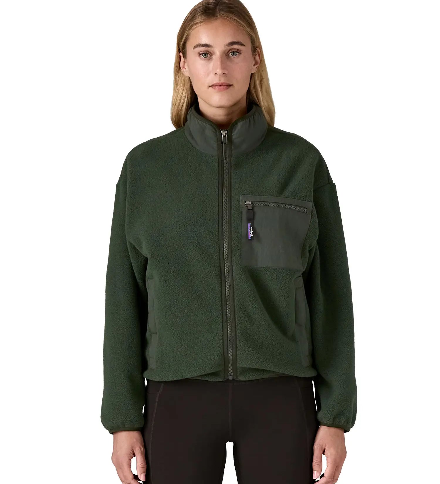 Woman wearing the Patagonia women's synchilla fleece jacket in dark green. Full zip jacket with zippered chest pocket and handwarmer pockets.