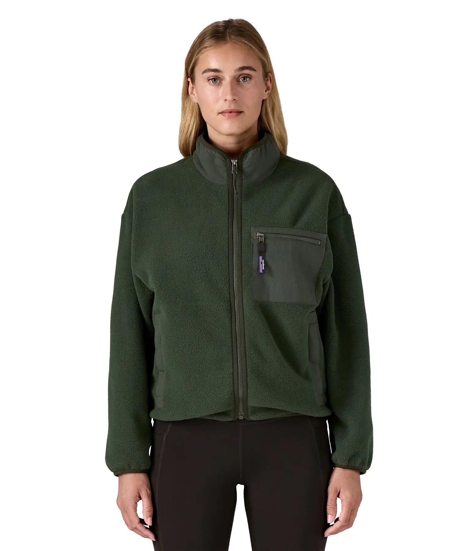 Woman wearing the Patagonia women's synchilla fleece jacket in dark green. Full zip jacket with zippered chest pocket and handwarmer pockets.