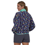 Woman wearing the Patagonia women's synchilla fleece in perennial purple with purple shorts, her back is facing and she is looking over her shoulder. The fleece is hip length and she has hands in pockets with the collar high. 