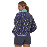 Woman wearing the Patagonia women's synchilla fleece in perennial purple with purple shorts, her back is facing and she is looking over her shoulder. The fleece is hip length and she has hands in pockets with the collar high. 