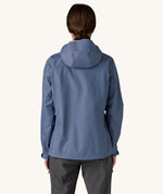 The back of a woman wearing the Patagonia Women's Torrentshell 3L Rain Jacket in a Current Blue colour. We have a wide range of Patagonia adult's and children's coats and clothing at Babipur.