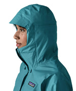 Close up of a womanwearing the Patagonia women's waterproof torrentshell 3L rain jacket in glacial blue with the hood up.