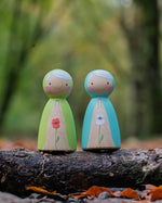 two hand painted peg dolls, one with a white poppy painted on its front, the other with a red poppy