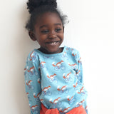 A child wearing the Pigeon Organics long sleeve top showing the fox riding a bicycle on turquoise organic cotton fabric