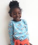 A child wearing the Pigeon Organics long sleeve top showing the fox riding a bicycle on turquoise organic cotton fabric