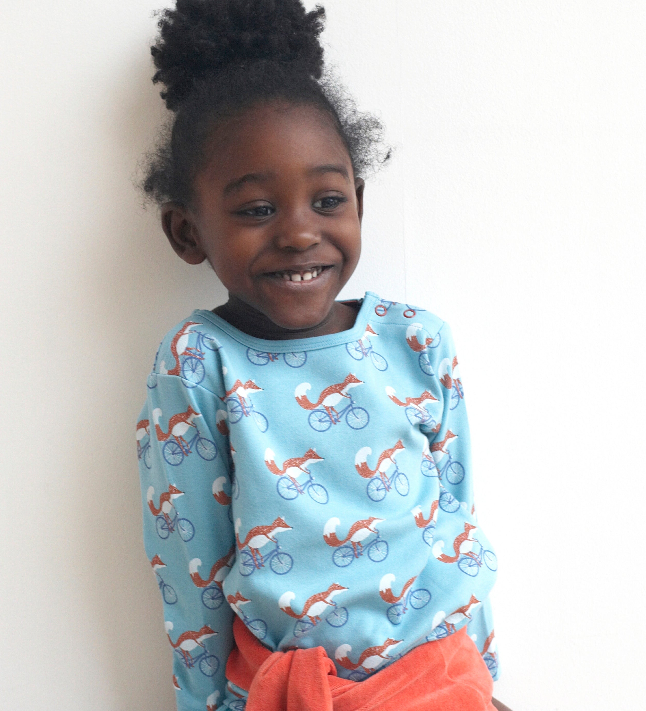 A child wearing the Pigeon Organics long sleeve top showing the fox riding a bicycle on turquoise organic cotton fabric