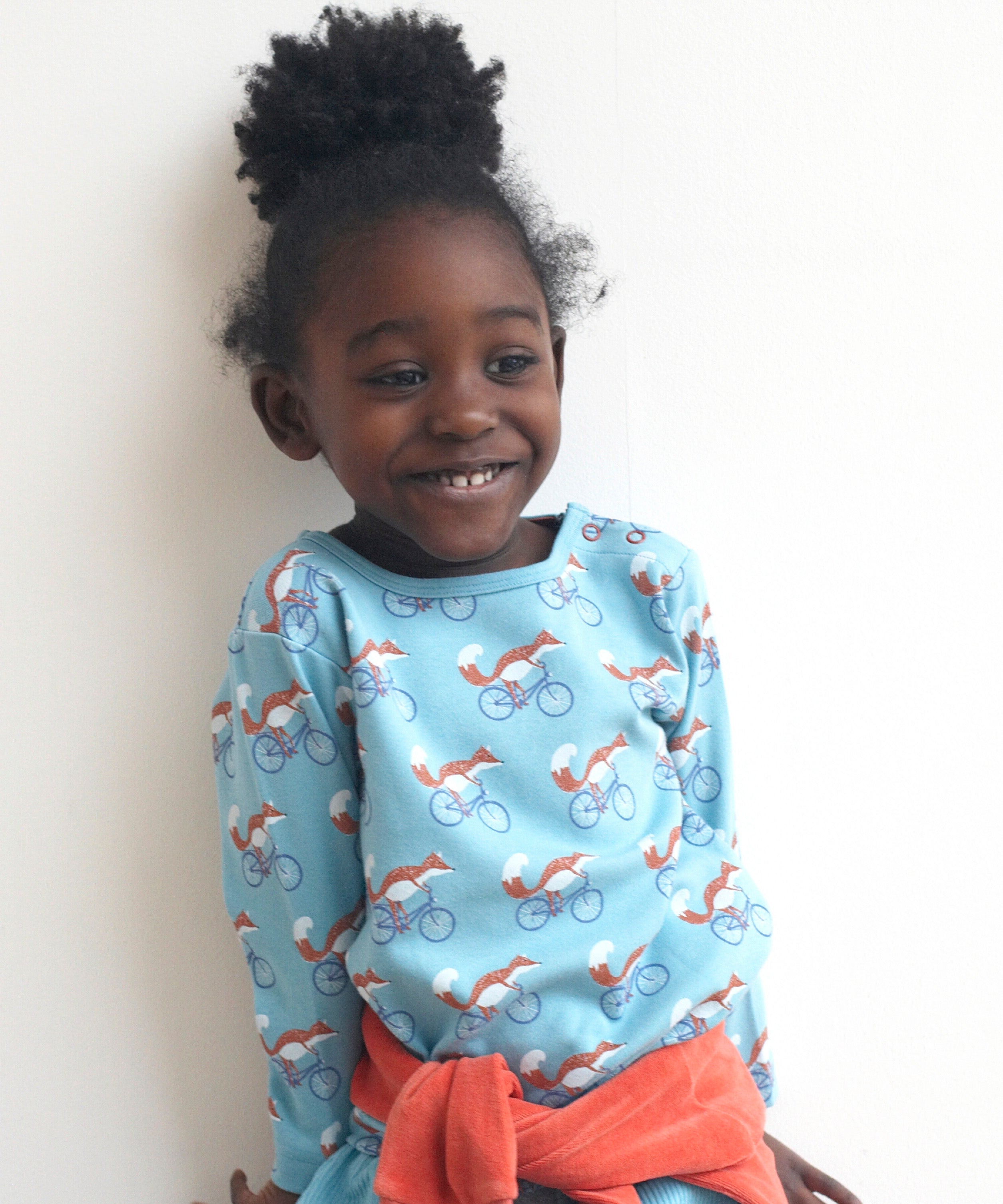 A child wearing the Pigeon Organics long sleeve top showing the fox riding a bicycle on turquoise organic cotton fabric
