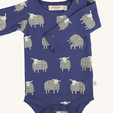 Pigeon Organics sheep body - GOTS organic cotton baby body in a navy blue colour, long sleeves and popper fasteners at the crotch for easy fitting. Features multiple prints of a playful standing white sheep 
