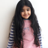 A child wearing the Pigeon Organics pink corduroy pinafore dress with a pink cat appliqué on the front pocket