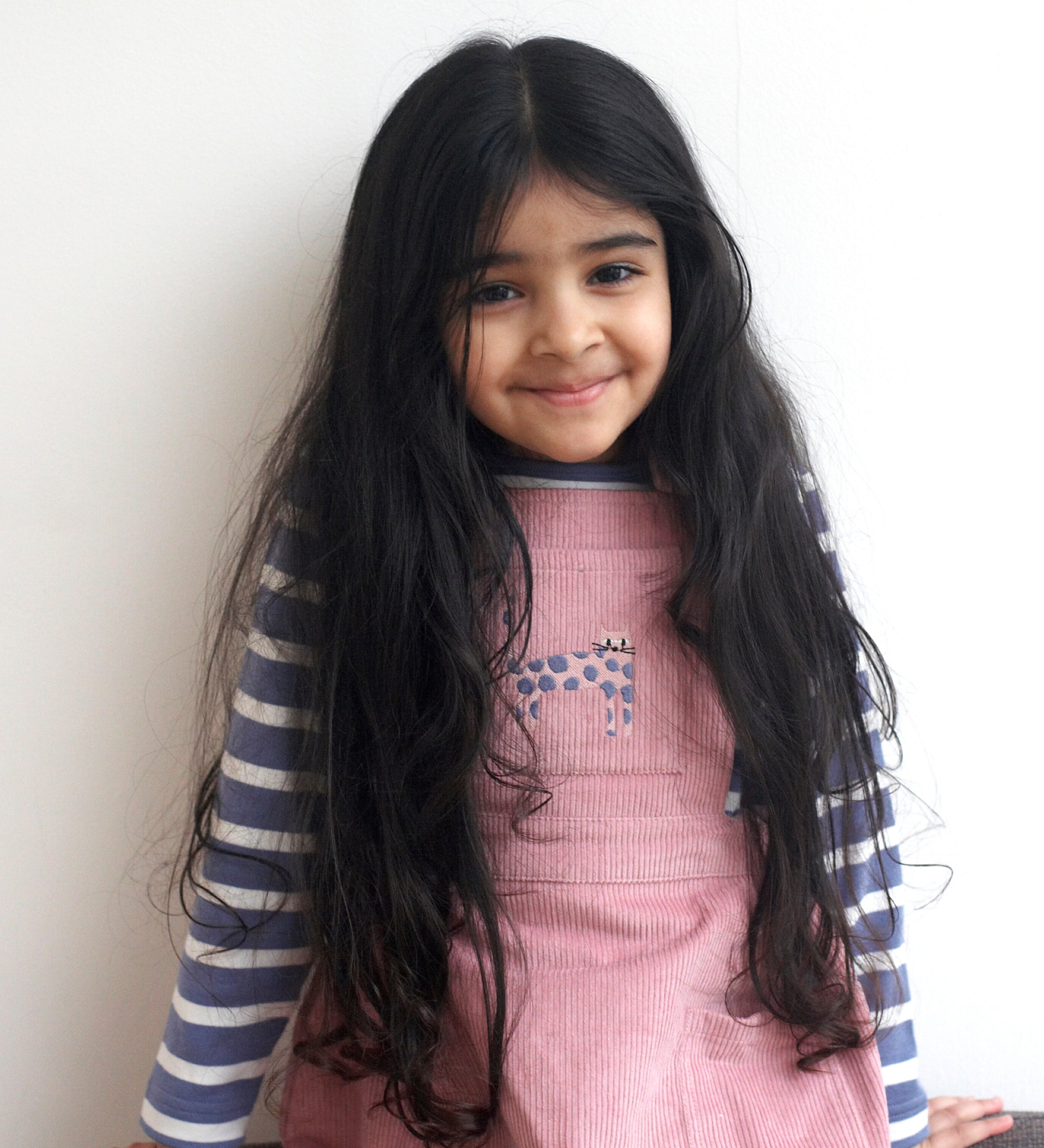 A child wearing the Pigeon Organics pink corduroy pinafore dress with a pink cat appliqué on the front pocket