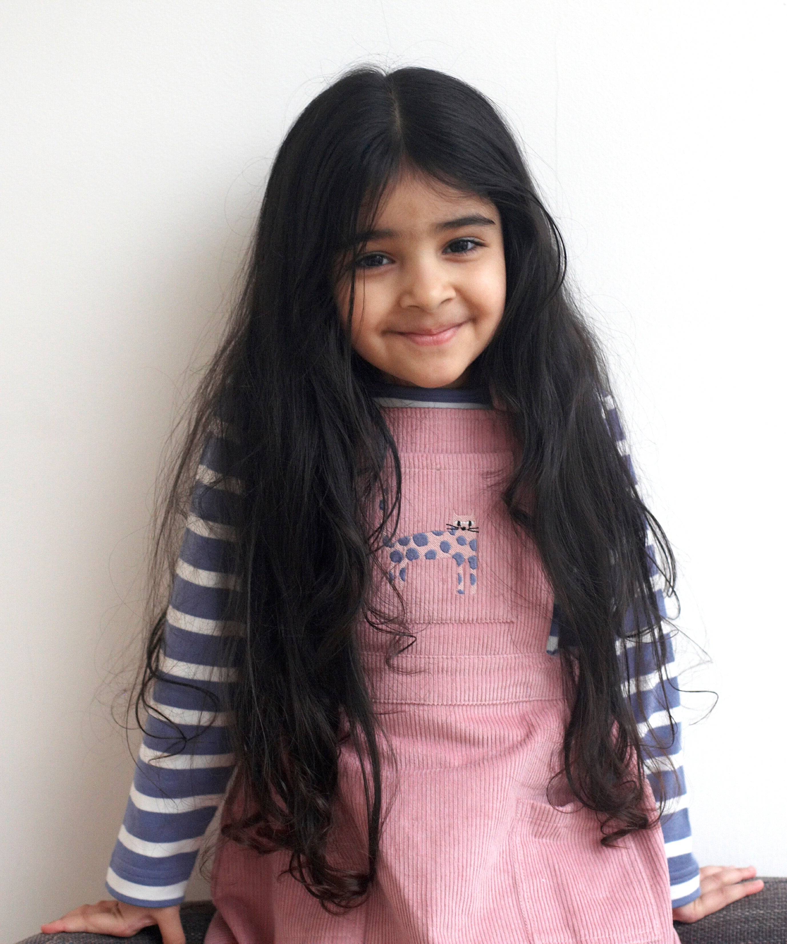 A child wearing the Pigeon Organics pink corduroy pinafore dress with a pink cat appliqué on the front pocket