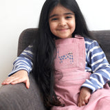 A child wearing the Pigeon Organics pink pinafore dress showing the corduroy detail and pink cat appliqué