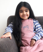 A child wearing the Pigeon Organics pink pinafore dress showing the corduroy detail and pink cat appliqué