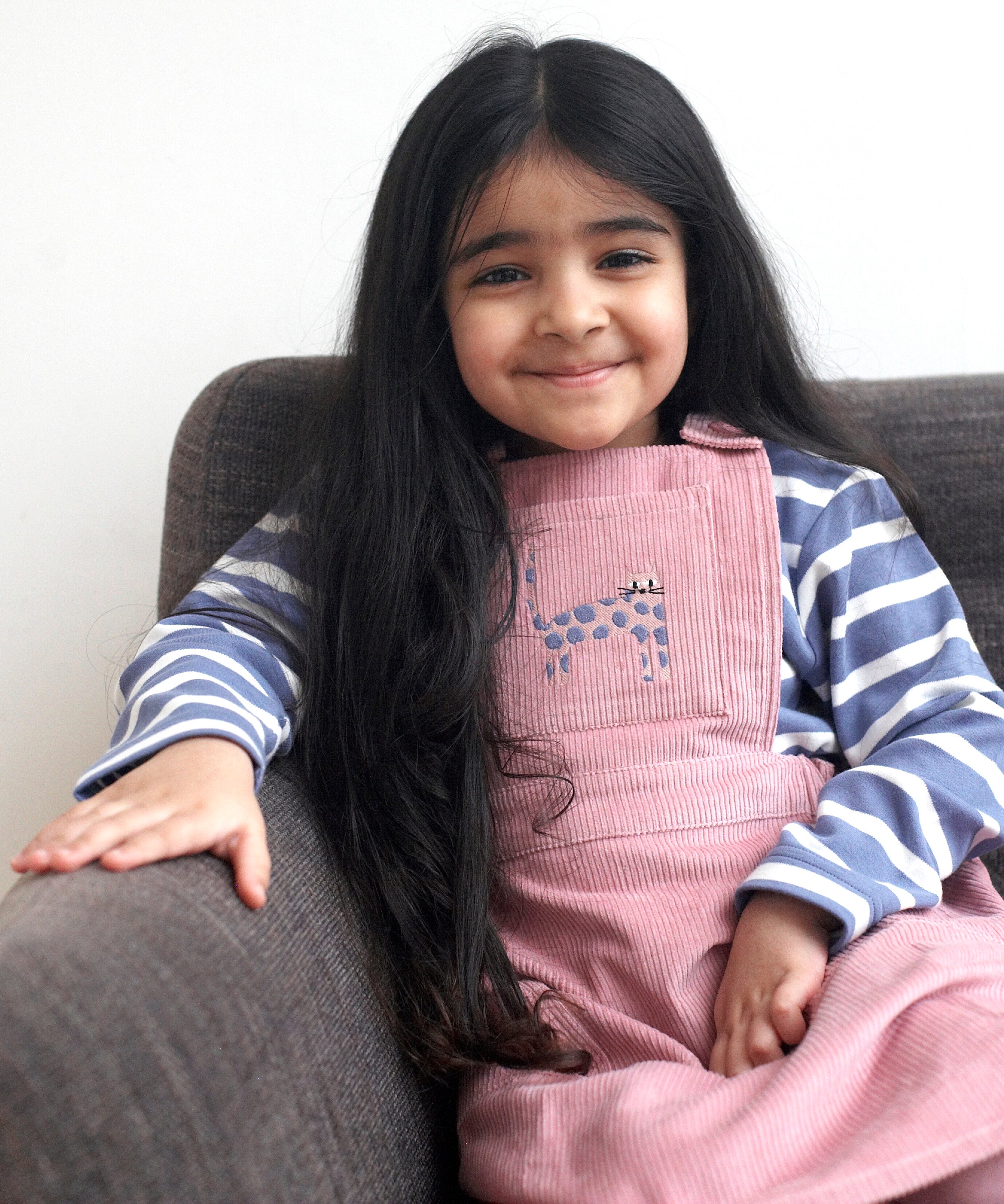 A child wearing the Pigeon Organics pink pinafore dress showing the corduroy detail and pink cat appliqué