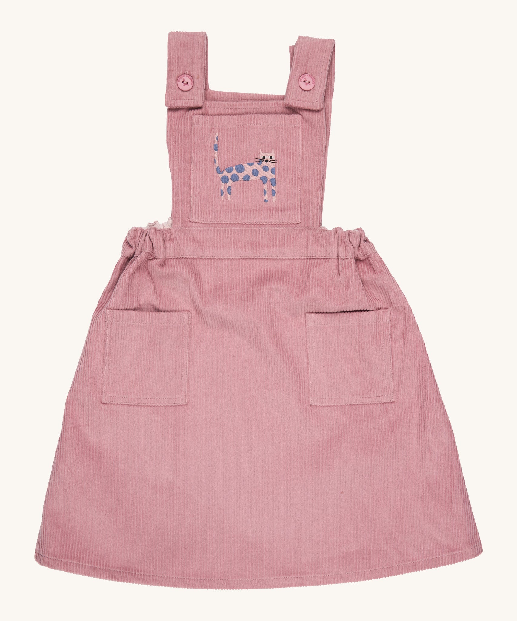 Pigeon Organics pinafore- GOTS organic cotton pinafore sleeves dress in pink corduroy. Features 2 small pockets at the front, button fasteners on the shoulders, an elasticated waist band and a pink cat embroidery on the chest.