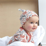 A close up of a baby sitting inside a trunk wearing the Pigeon Organics kimono romper and the knotted hat. Showing the squirrel and floral print on organic cotton fabric