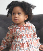 Close up of the Pigeon Organics squirrel smock dress worn by a toddler showing the soft elasticated waist band and collar detail.
