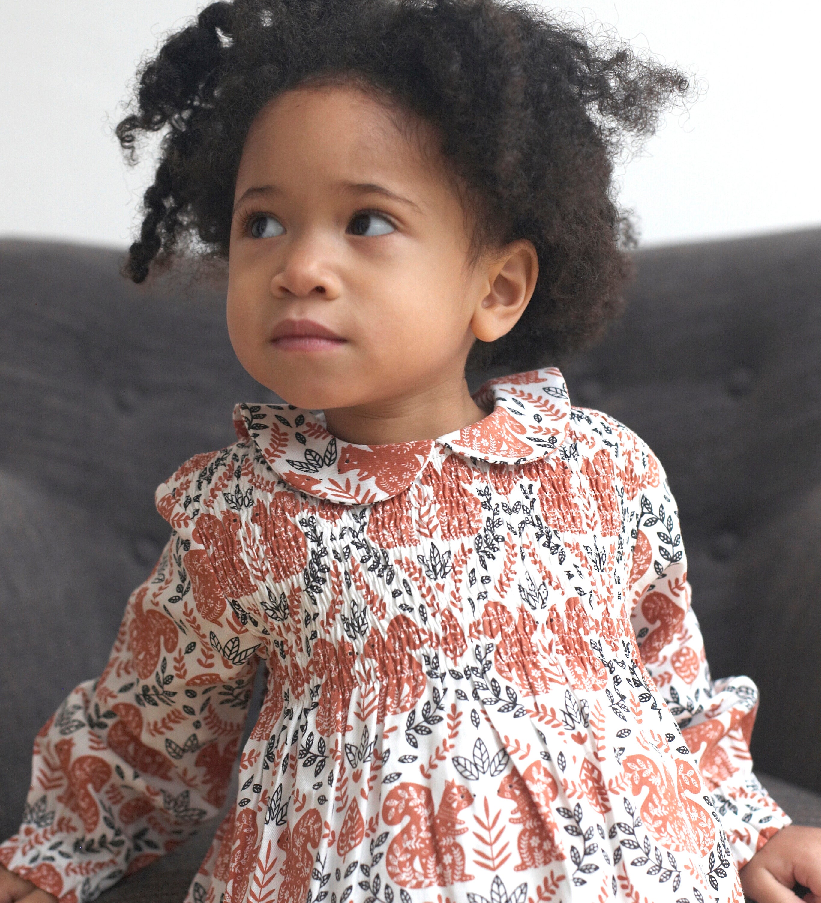 Close up of the Pigeon Organics squirrel smock dress worn by a toddler showing the soft elasticated waist band and collar detail.